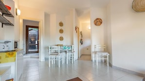 A spacious living area with a dining table and chairs, a kitchen area with appliances, and a hallway leading to another room.