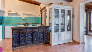 A kitchen with a tiled backsplash, a wooden cabinet with glass doors, and a white refrigerator. - Villetta Hemingway (Trinità d'Agultu e Vignola)
