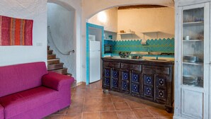 A kitchen with a tiled backsplash, a wooden cabinet with glass doors, and a red sofa. - Villetta Hemingway (Trinità d'Agultu e Vignola)