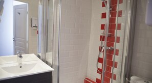 Ein Badezimmer mit Duschkabine aus Glas, einem weißen Waschbecken und Fliesenwänden.