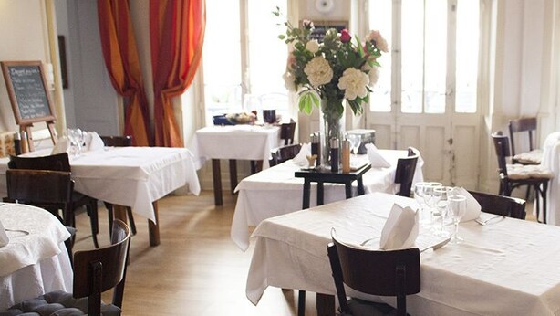 Un comedor con mesas listas para el servicio, un menú en una pizarra y un jarrón con flores.