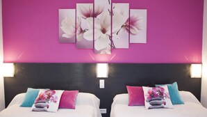 Habitación de hotel con dos camas, cada una con un edredón blanco y varios almohadones, incluyendo diseños florales. La habitación tiene una pared rosa grande con una obra de arte floral y dos lámparas de pared.