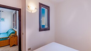 A bedroom with a bed, a bedside table, a wall-mounted light, and a window with a view.