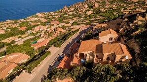An aerial view of a coastal town with terracotta-roofed buildings, a road, and a view of the sea.