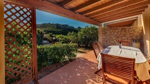 A covered patio with a table and chairs, stone walls, and a view of the surrounding landscape. - Villetta Orchidea (Trinità d'Agultu e Vignola)