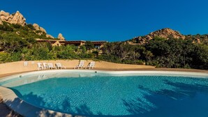A clear blue pool with white lounge chairs and a building with a tiled roof in the background. - Villetta Orchidea (Trinità d'Agultu e Vignola)