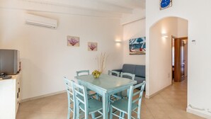 A dining area with a table and chairs, a sofa, and artwork on the walls. - Villetta Orchidea (Trinità d'Agultu e Vignola)