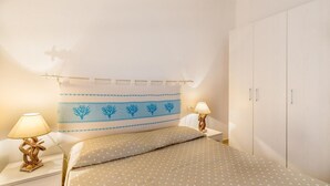 A bedroom with a bed, two bedside tables, two lamps, a headboard with a decorative pattern, and a wardrobe. - Villetta Orchidea (Trinità d'Agultu e Vignola)
