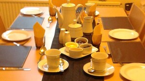 A dining table set with plates, cups, and a teapot, with a window in the background. - St Hilda Guest House (Bridlington)