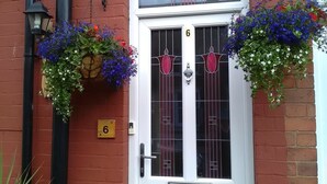 A white door with the number 6, flanked by hanging flower baskets and a black lamp post. - St Hilda Guest House (Bridlington)