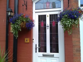 A white door with the number 6, flanked by hanging flower baskets and a black lamp post.