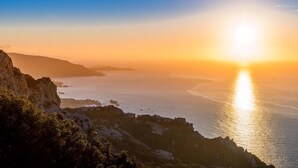 A coastal sunset view with rocky terrain and a clear sky.