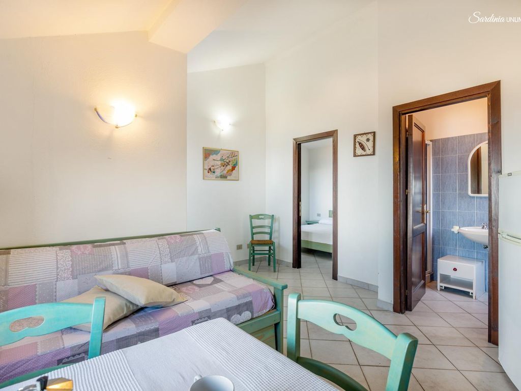 Une chambre à coucher avec un lit, une chaise, une table et une salle de bain visible à travers une porte ouverte.