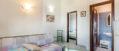 Une chambre à coucher avec un lit, une chaise, une table et une salle de bain visible à travers une porte ouverte.