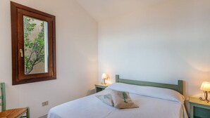 A bedroom with a bed, two bedside tables with lamps, a chair, and a framed picture on the wall.