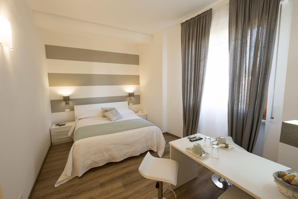A hotel room with a bed, bedside tables, a desk, and a chair.