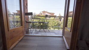 A room with a wooden floor, a small table with chairs, and a view of a house through a window. - Suite Simonetta (Sarzana)