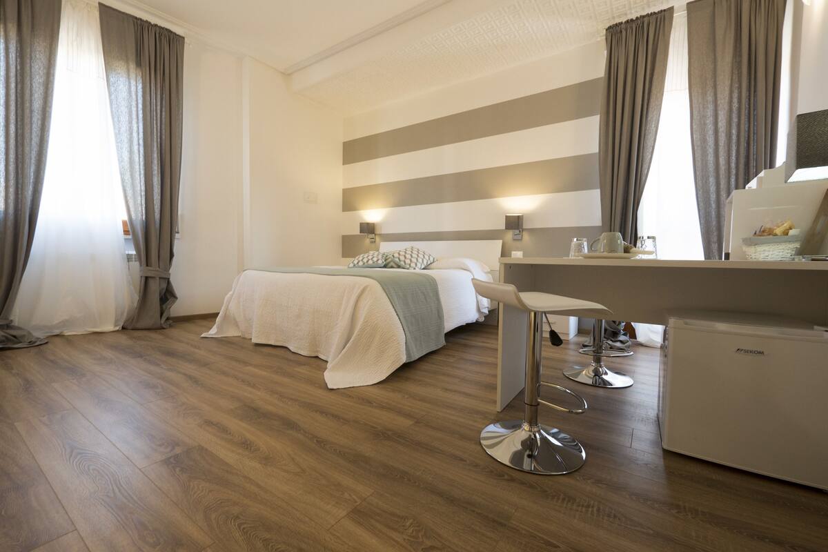 A hotel room with a bed, a desk, a chair, and a minibar.