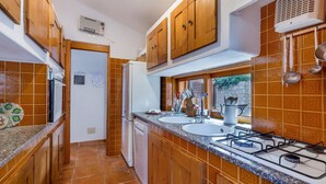 A kitchen with wooden cabinets, a gas stove, two sinks, and a refrigerator. - Villa Mariù e Amelie (Aglientu)