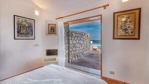 A bedroom with a bed, a stone wall, and a view of the sea. - Villa Mariù e Amelie (Aglientu)