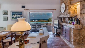 A room with a view of the sea, a stone fireplace, and a dining area with a table and chairs. - Villa Mariù e Amelie (Aglientu)