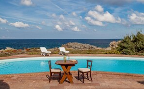 A poolside area with a table and chairs, overlooking the ocean.