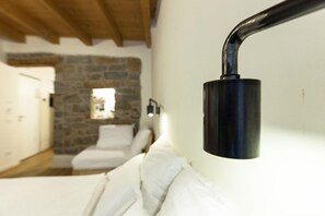 A bed with white linens in a room with a stone wall and wooden beams. - Locanda alle Beccherie (Trieste)