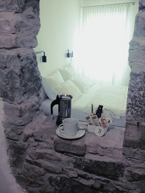 A stone-walled room with a bed, a coffee maker, a cup, and a tray with breakfast items. - Locanda alle Beccherie (Trieste)