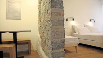 A room with a stone wall, a white sofa, a wooden table, and two wall-mounted lamps.