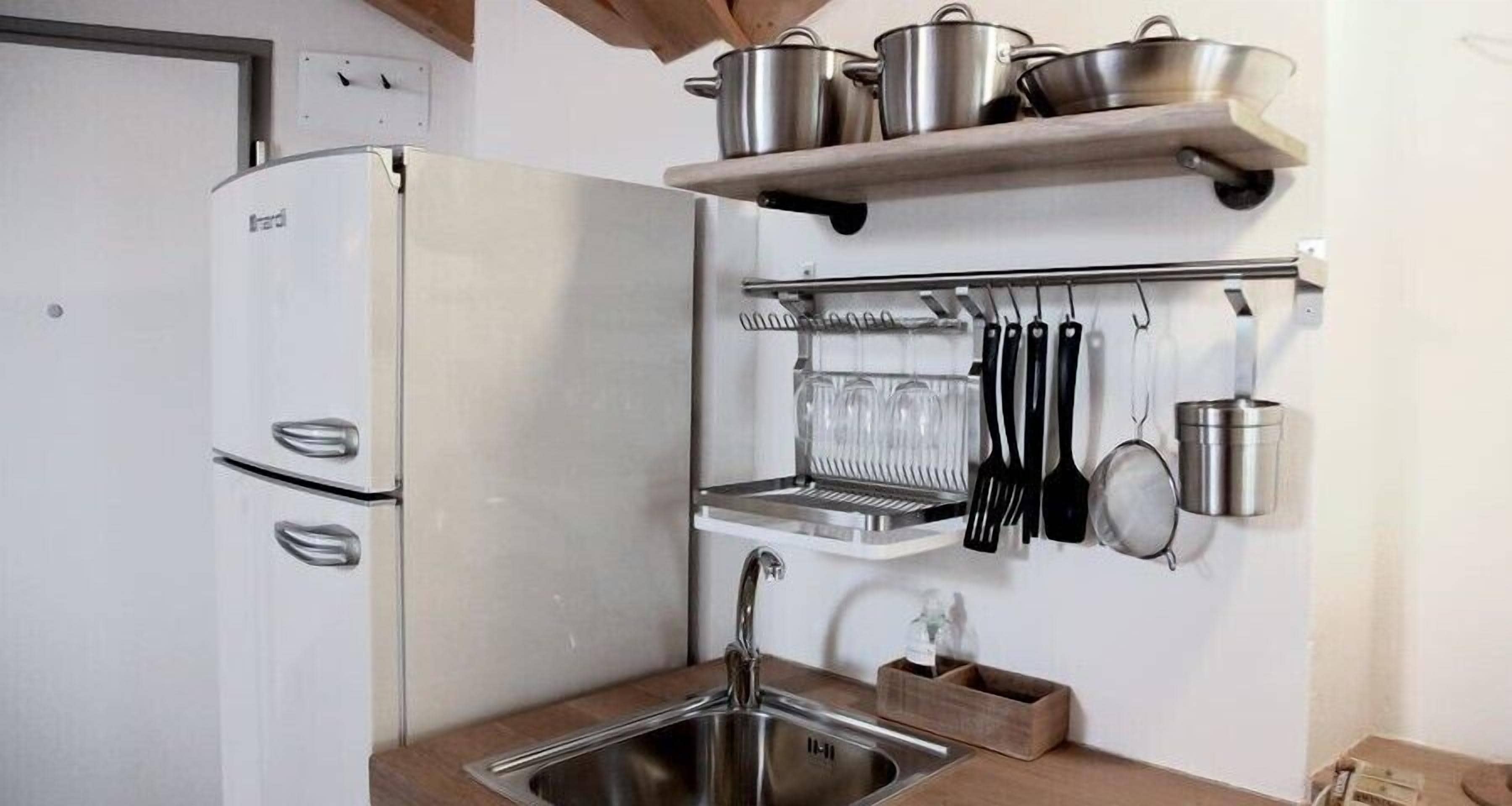 A compact kitchen with a built-in refrigerator, a stainless steel sink, and a utensil rack.