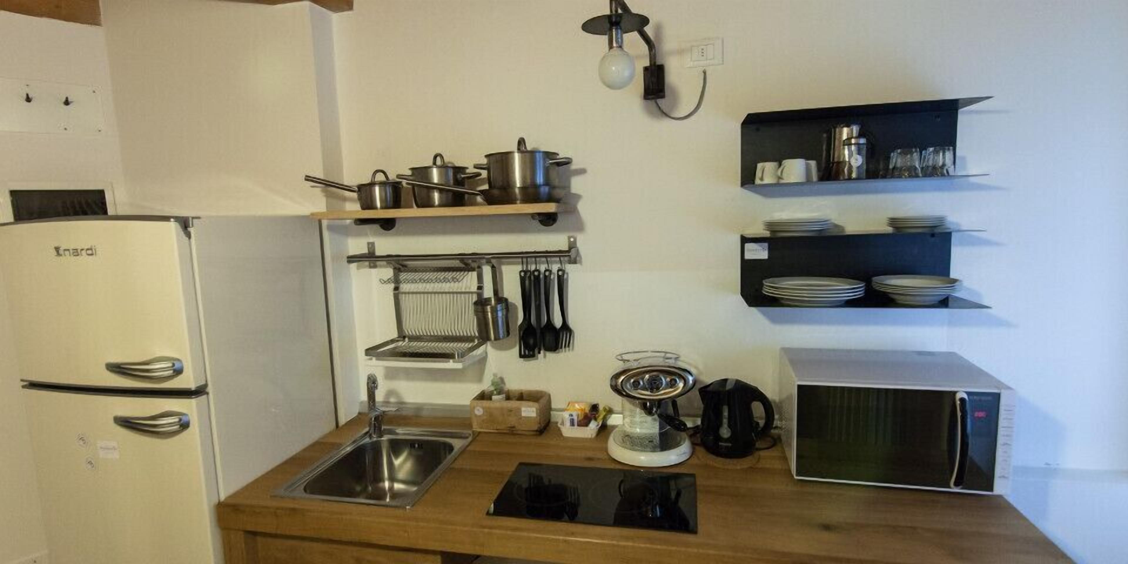 A compact kitchen with a white refrigerator, a microwave, and a sink. There are shelves above the counter holding dishes and utensils.