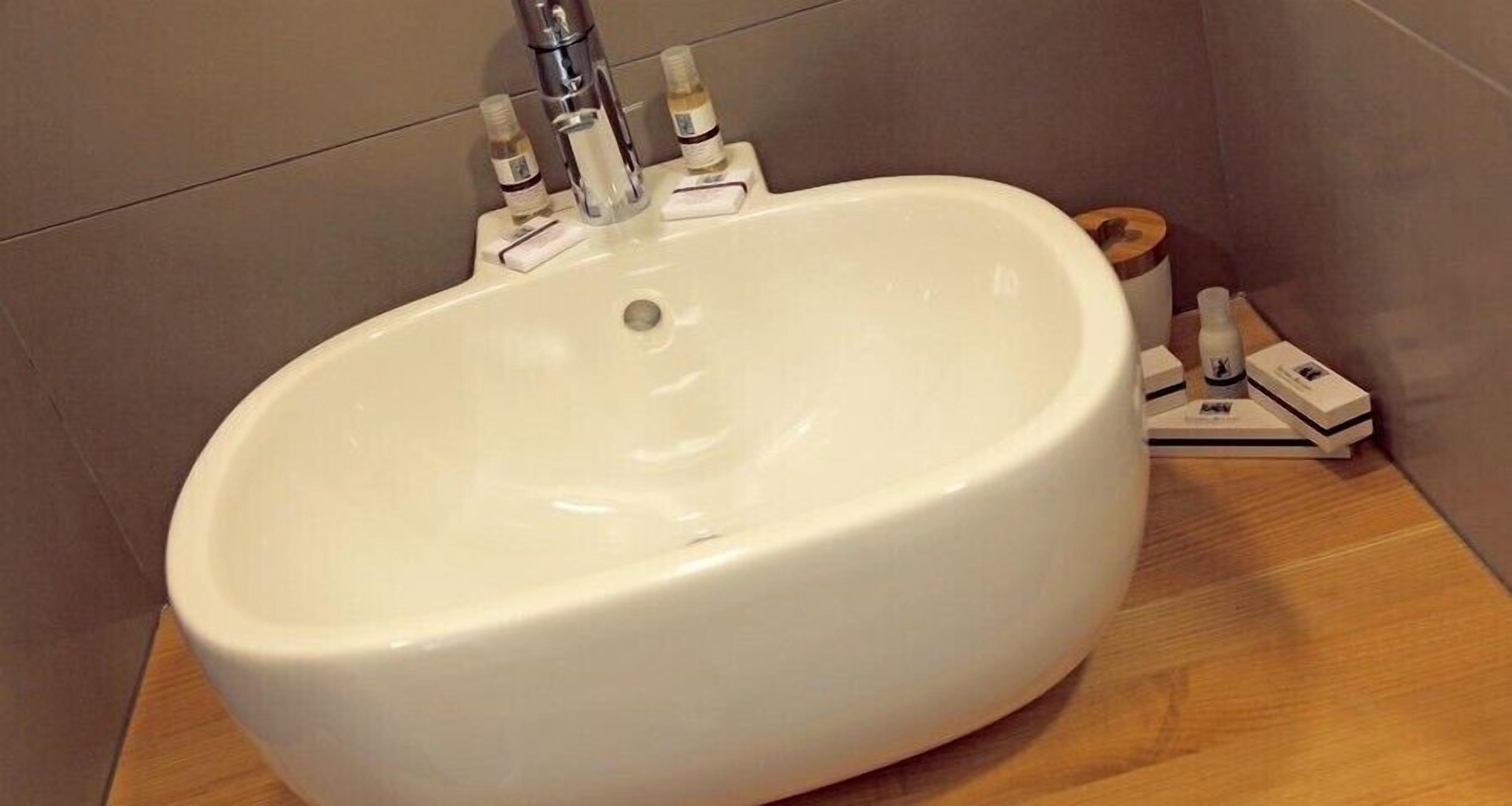 Ein weißes Waschbecken mit einem Wasserhahn, zwei Seifenspendern und einer hölzernen Seifenschale in einem Badezimmer.