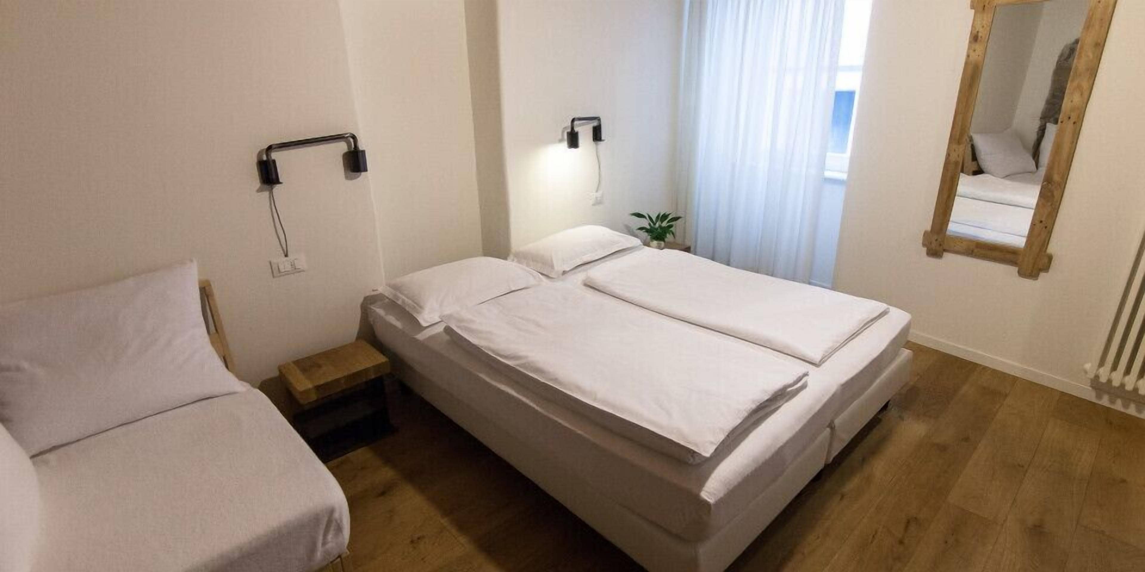 Une chambre à coucher avec un lit double, une table de chevet, une lampe, un miroir et une fenêtre avec des rideaux.