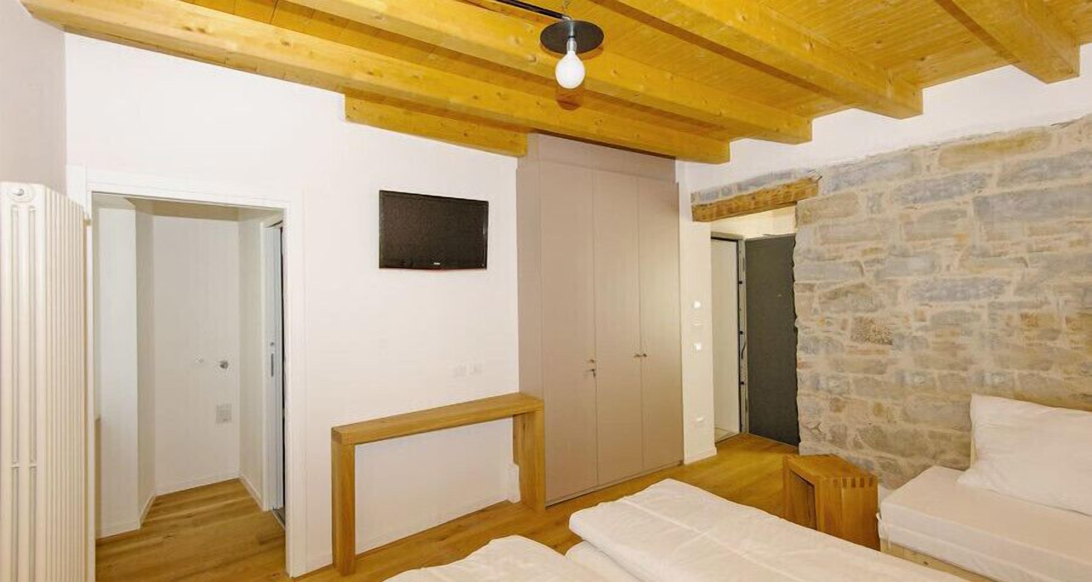 A bedroom with a stone wall, wooden ceiling beams, a bed, a bedside table, and a wardrobe.