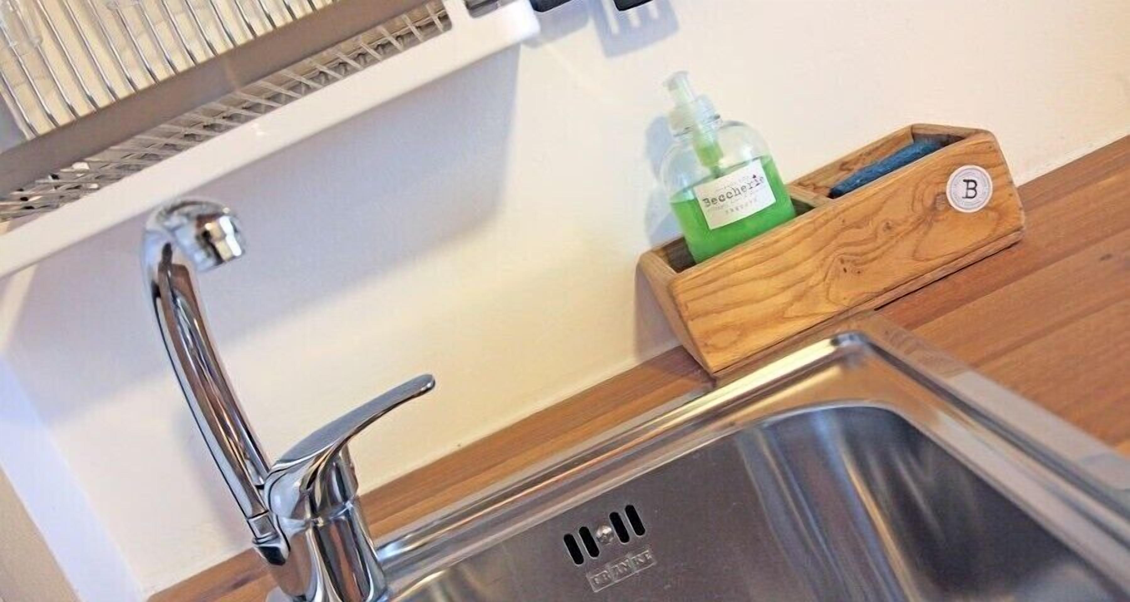 A stainless steel kitchen sink with a faucet, a wooden soap dish with a bottle of liquid soap, and a wooden box with a letter 'B'.