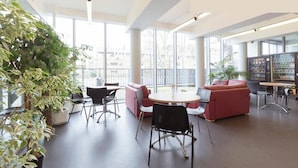 A modern indoor space with large windows, a round table, red sofas, and black chairs. - Davies Court - Hostel (London)