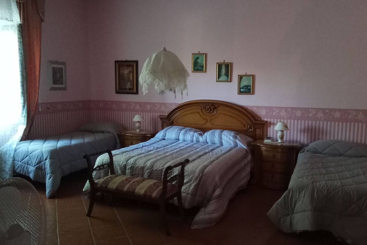 Ein Schlafzimmer mit zwei Einzelbetten, einem Holzstuhl, einem Nachttisch mit Lampe und gerahmten Bildern an der Wand.