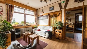Una sala de estar acogedora con sofá, sillón, mesa de centro, pisos de madera y ventanas amplias con cortinas.