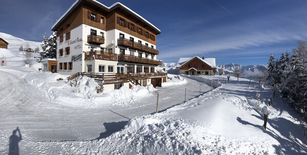 Ein mehrstöckiges Hotel mit Balkonen, im Hintergrund eine Skipiste und ein klarer Himmel.