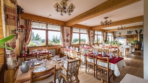 Un restaurante con interiores de madera, varias mesas dispuestas para comer y grandes ventanales con vistas a zonas verdes.
