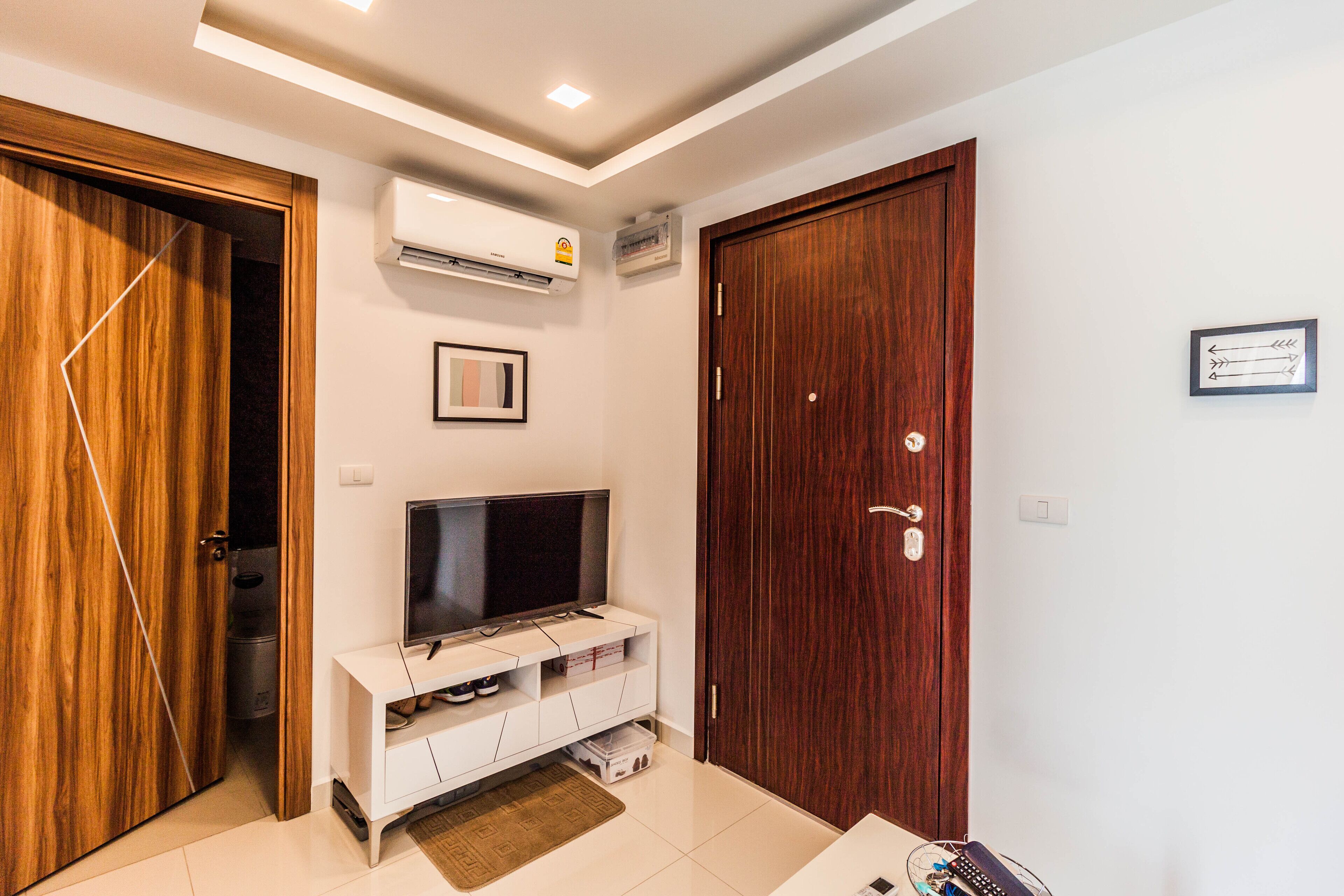 A modern living room with a flat-screen TV on a white console, a wooden door, and a closed wardrobe.