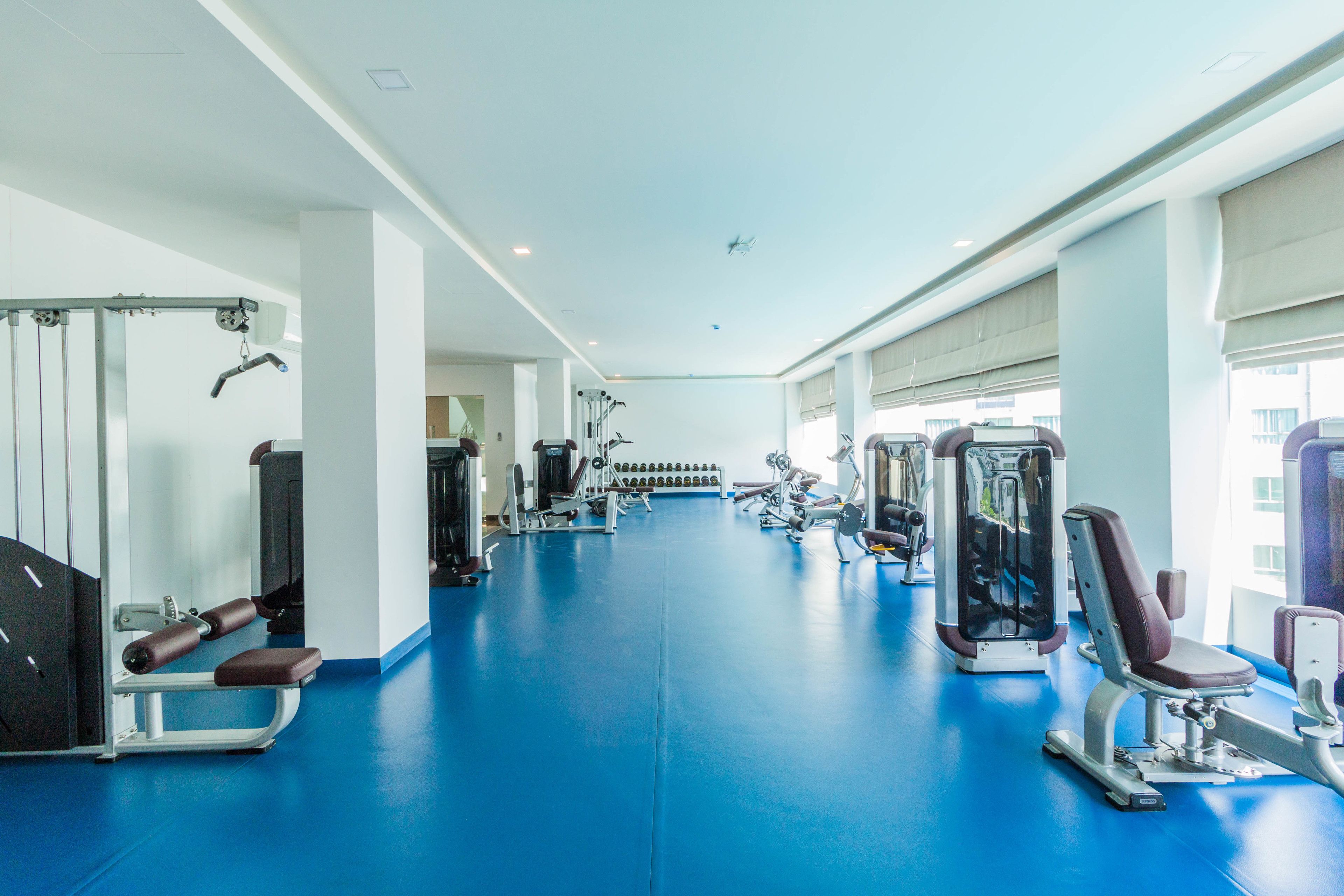A gym with exercise equipment, a blue floor, and large windows.