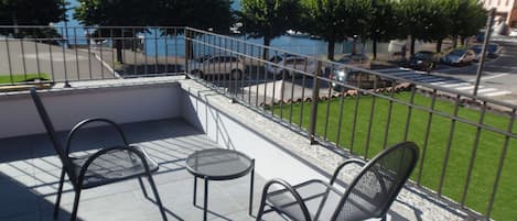A balcony with two chairs and a small table, overlooking a body of water and mountains.