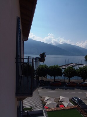A balcony with a view of a lake and mountains, a parking area with cars, and outdoor umbrellas. - Albergo Dongo (Dongo)