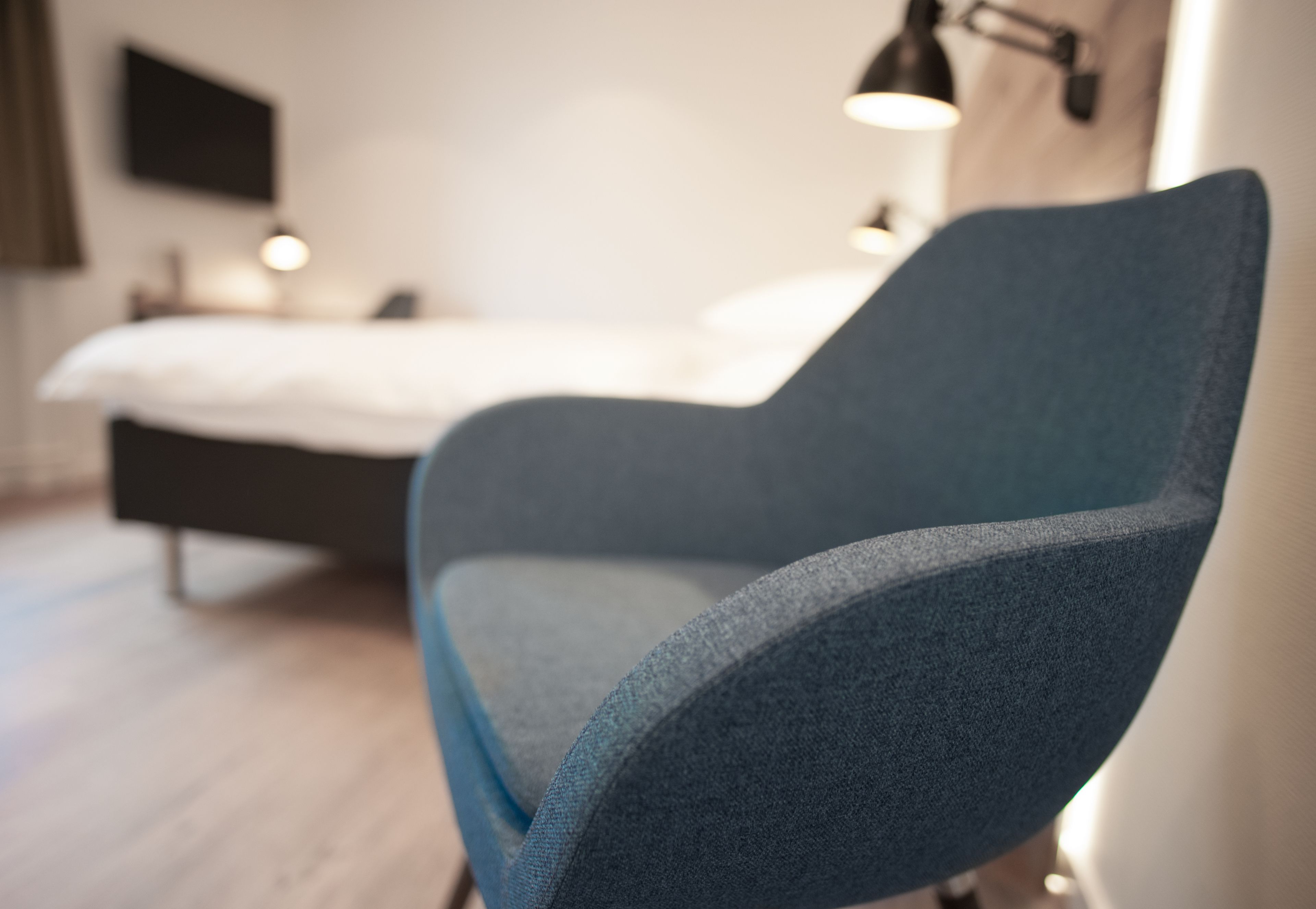 Ein modernes Zimmer mit einem Bett, einem blauen Sessel und einem Nachttisch.