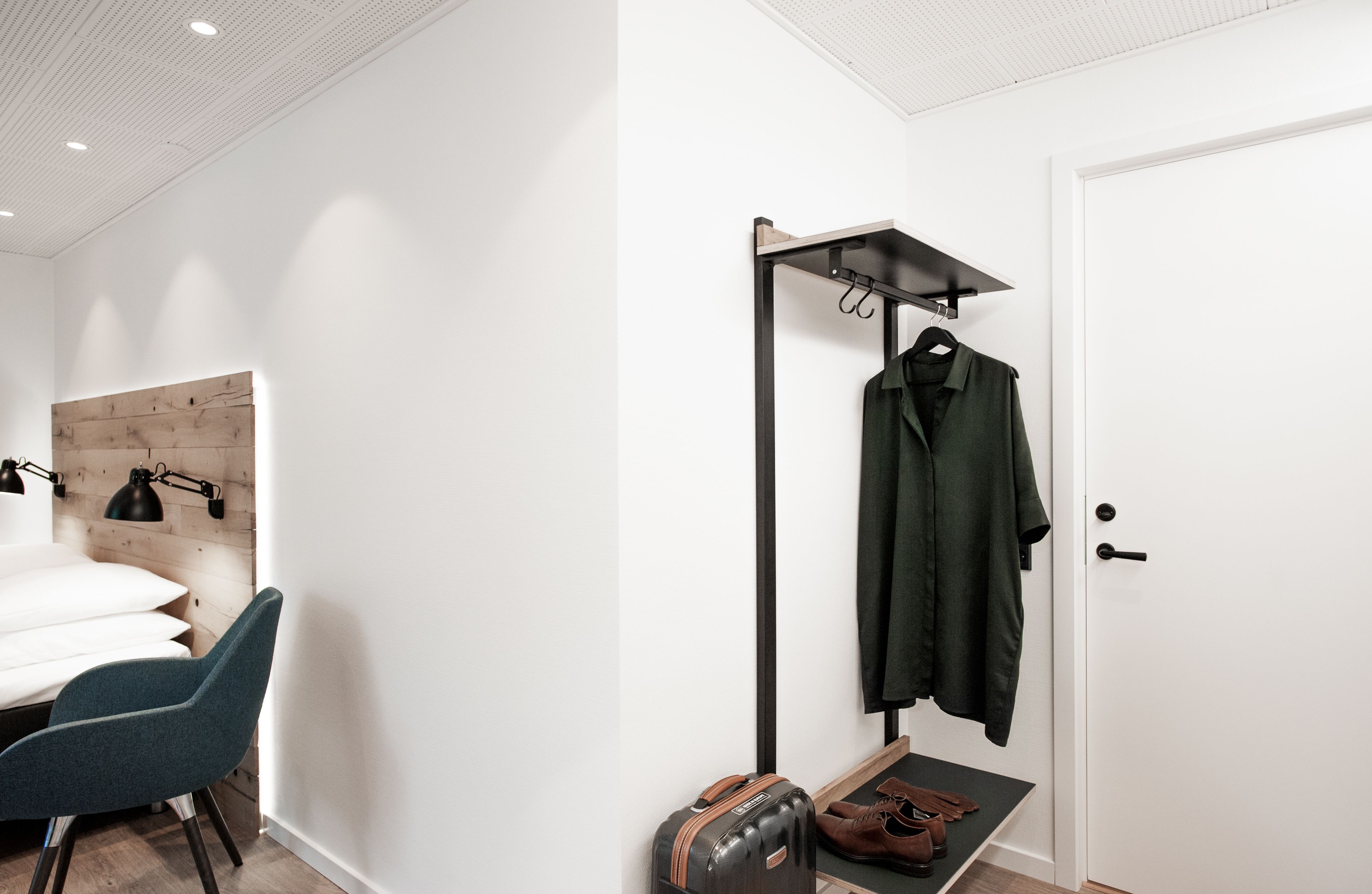 A modern room with a bed, a desk, a chair, a coat rack, and a door.
