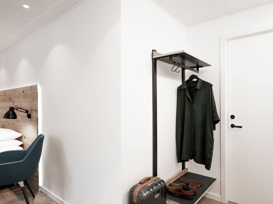 Una camera moderna con un letto, una scrivania, una sedia, un appendiabiti e una porta.