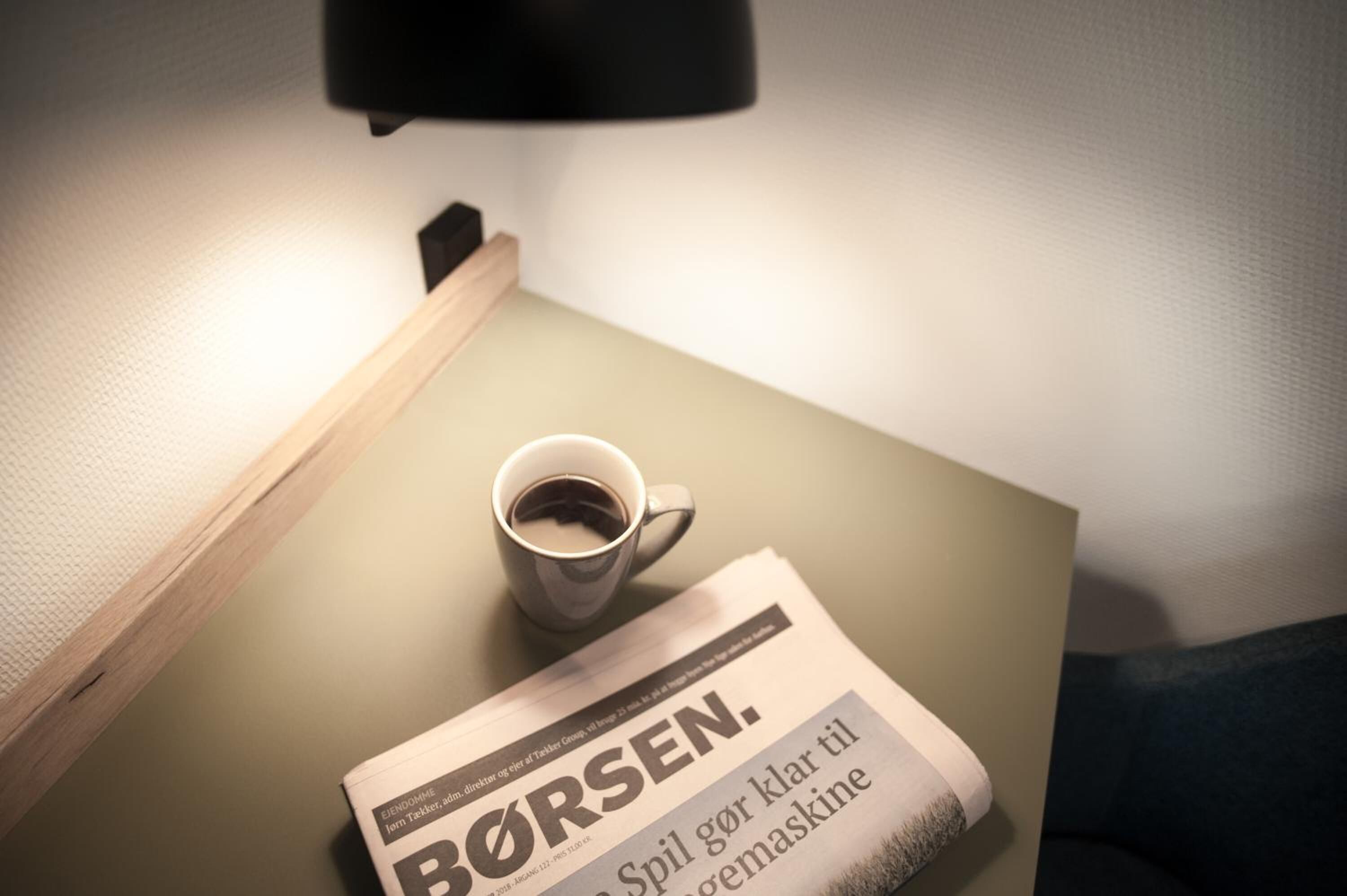 Un journal dont la une affiche le titre « BØRSEN », posé sur une table à côté d’une tasse de café.
