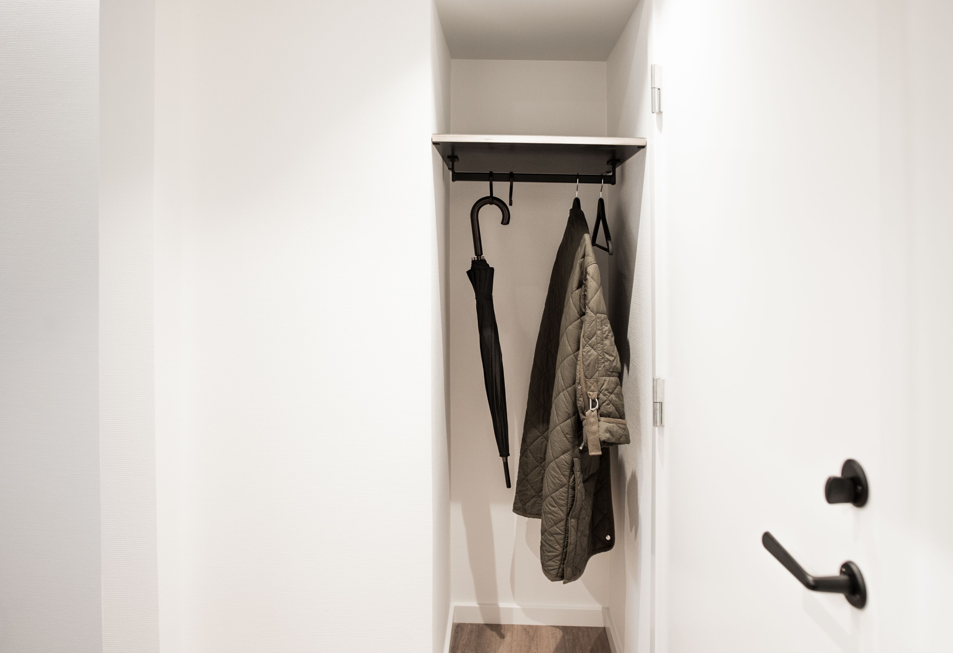 A narrow hallway with a coat rack holding a jacket and an umbrella.