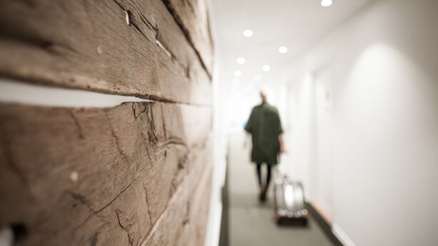 A corridor with a wooden wall and a person walking away carrying a suitcase. - Hotel Town Living (Ringkobing)